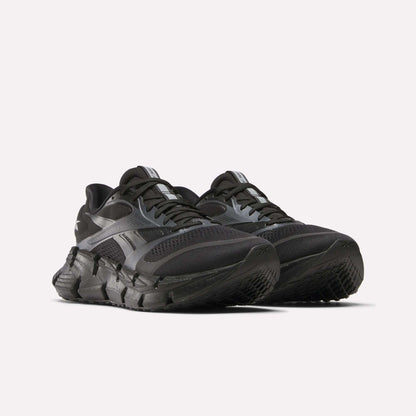 A pair of black Reebok Men's FloatZig 2 Running Shoes with thick, textured soles and mesh uppers, featuring energy-returning cushioning, are positioned side by side on a white background.