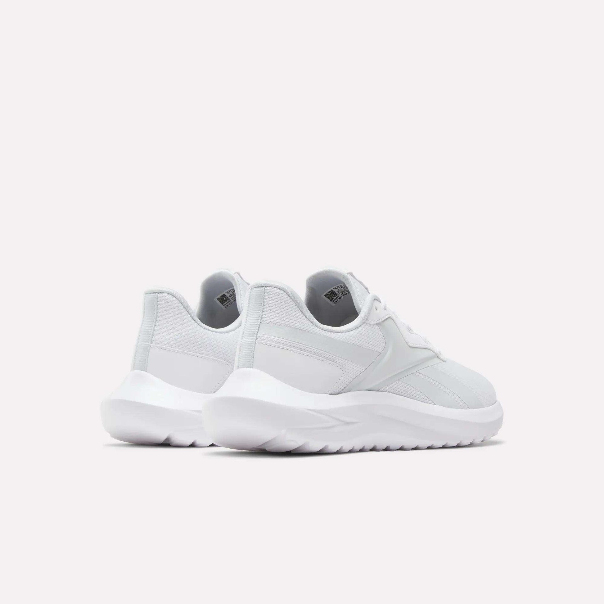 The Reebok Women's Energen Lux Running Shoes are shown in white from the back and side on a plain light background, highlighting their versatile style, thick textured soles, and comfort.