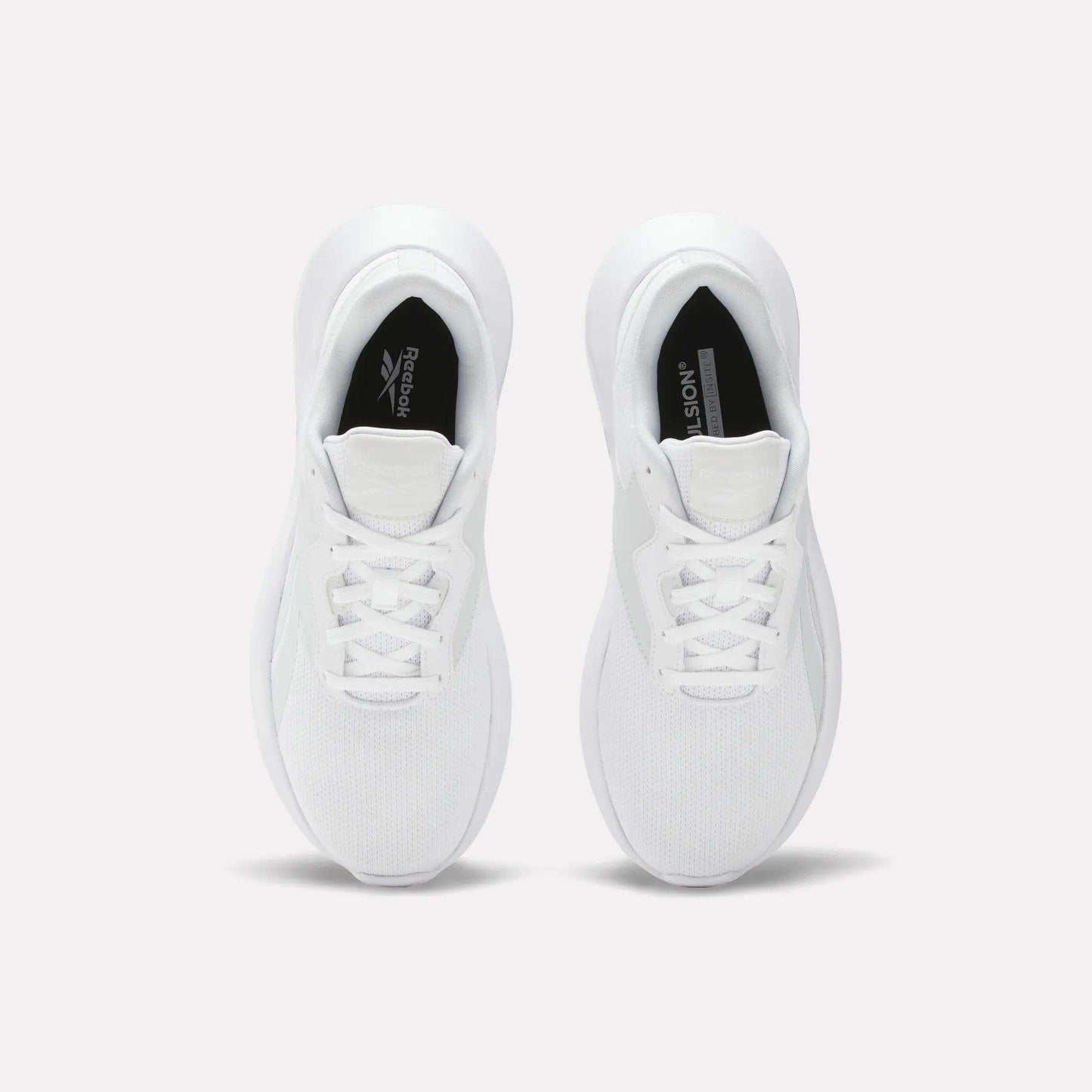 A pair of Reebok Women's Energen Lux Running Shoes viewed from above displays laces, mesh toe texture, and black Reebok logos on the inner soles. These lightweight shoes are side by side on a plain light background.