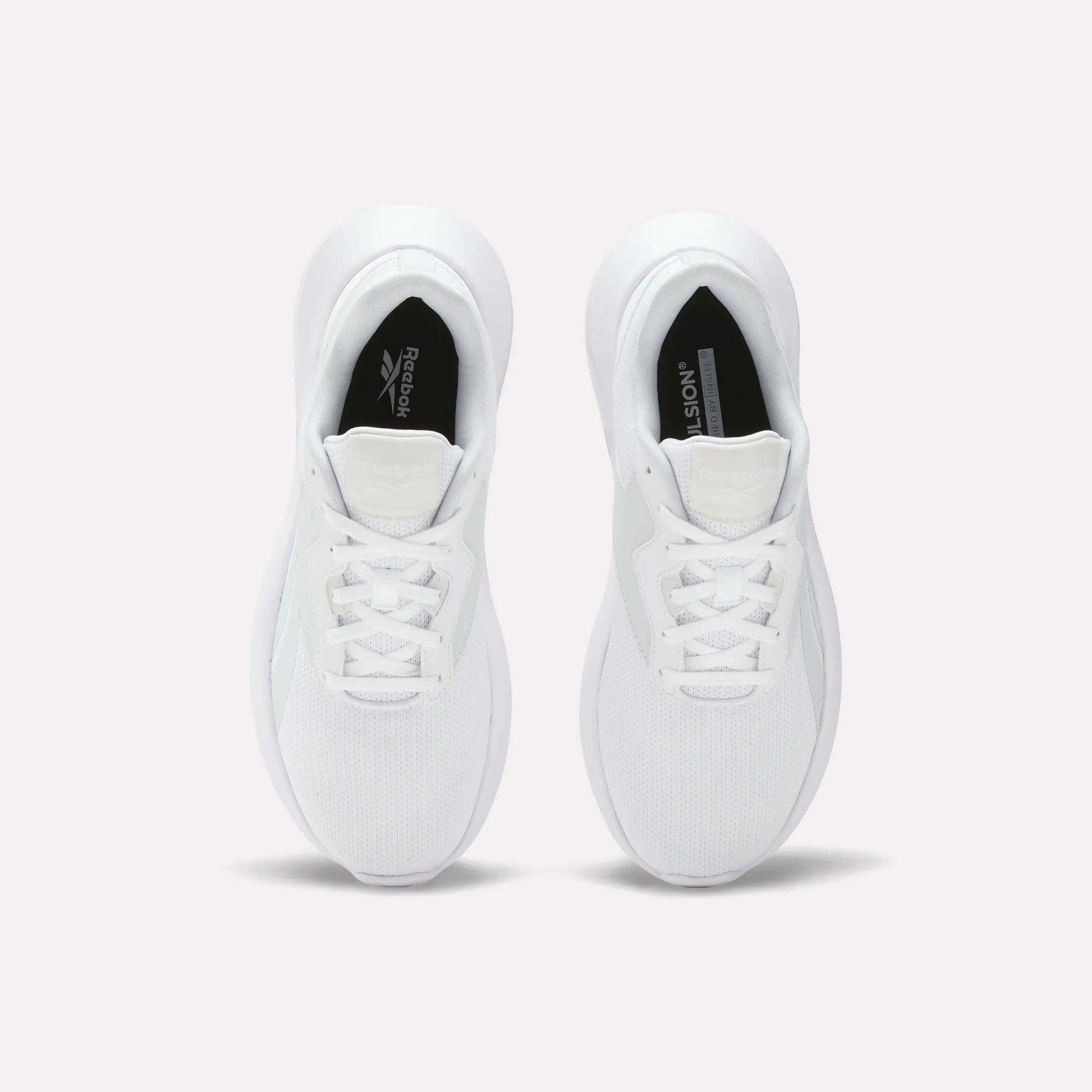 A pair of Reebok Women's Energen Lux Running Shoes viewed from above displays laces, mesh toe texture, and black Reebok logos on the inner soles. These lightweight shoes are side by side on a plain light background.