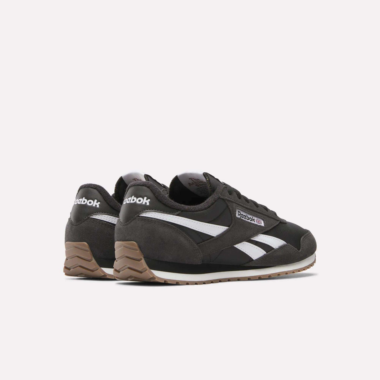The Reebok Classic AZ Shoes feature a black design with white stripes, brown suede heel accents, and gum rubber soles, blending ’70s retro style with modern comfort, shown against a plain white background.