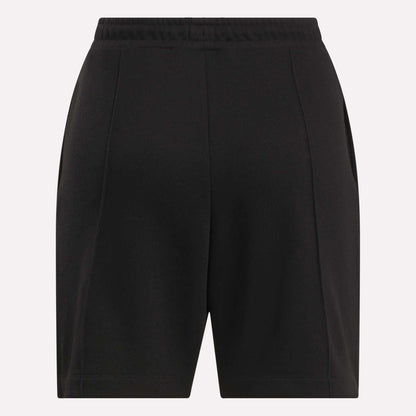 Reebok Women's Pintuck Long Shorts in black, featuring an elastic waistband, front pleats, and side pockets, made from a soft cotton-blend fleece. Displayed against a plain light background.