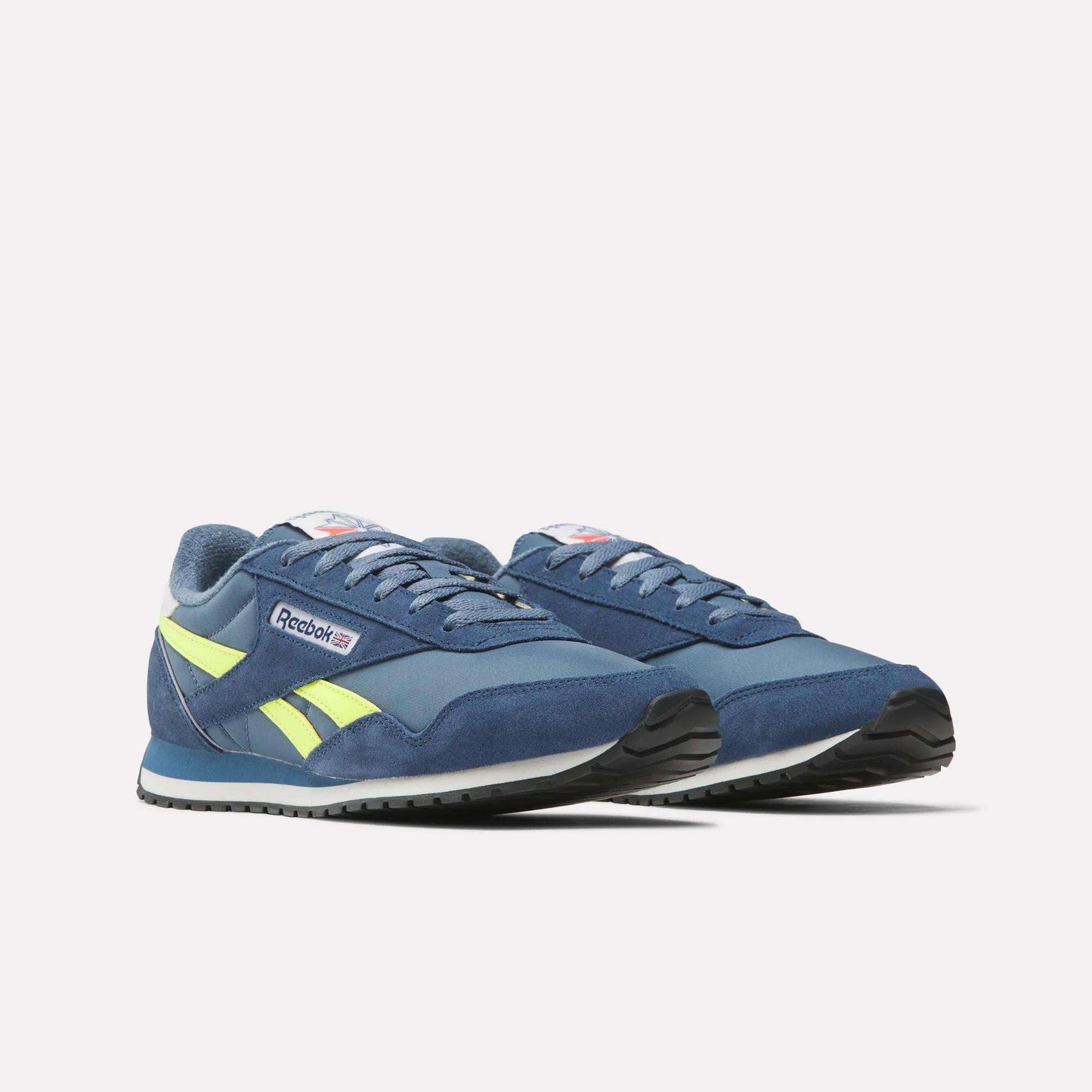 A pair of Classic AZ Shoes by Reebok in blue with yellow accents and white soles, displayed on a plain white background. Shown at an angle to highlight their ‘70s-inspired retro running style.