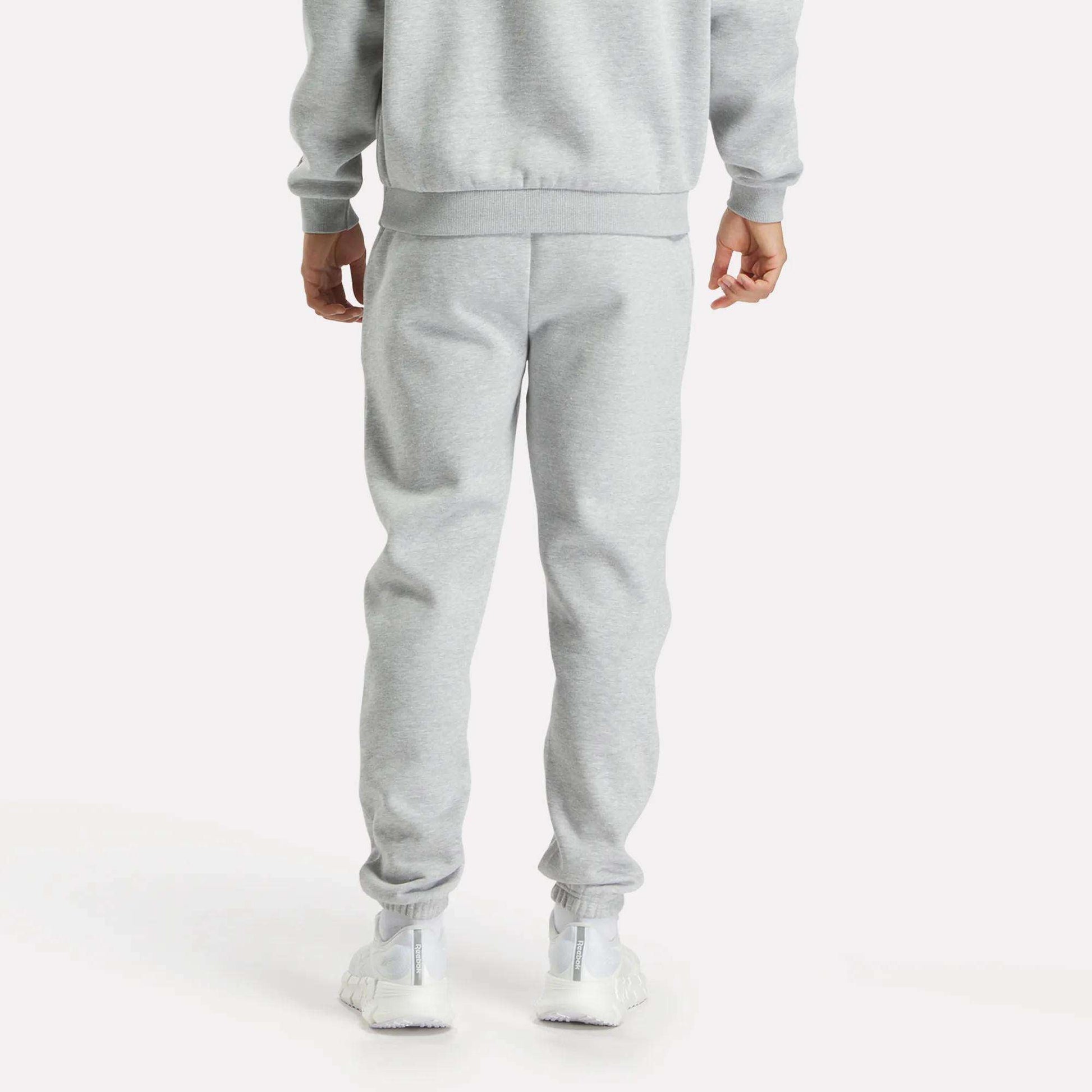 A person faces away, wearing Reebok Men's Joggers in light gray with a matching sweatshirt and white sneakers, set against a plain white background.