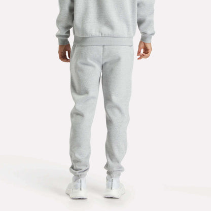 A person faces away, wearing Reebok Men's Joggers in light gray with a matching sweatshirt and white sneakers, set against a plain white background.