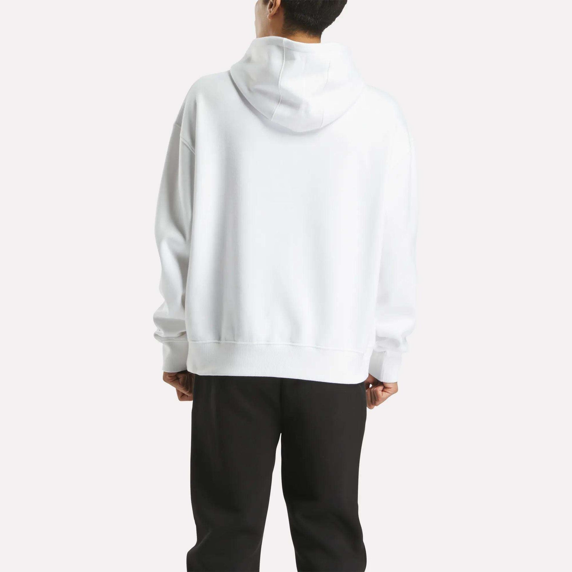 A man faces away from the camera, wearing a Reebok Men's Hoodie in plain white with the hood up and black pants, set against a light background.