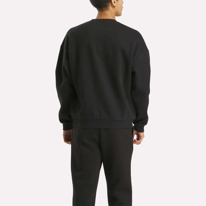 A person stands with their back to the camera wearing the Reebok Men's Cottle Sweatshirt and matching black pants against a plain light background.