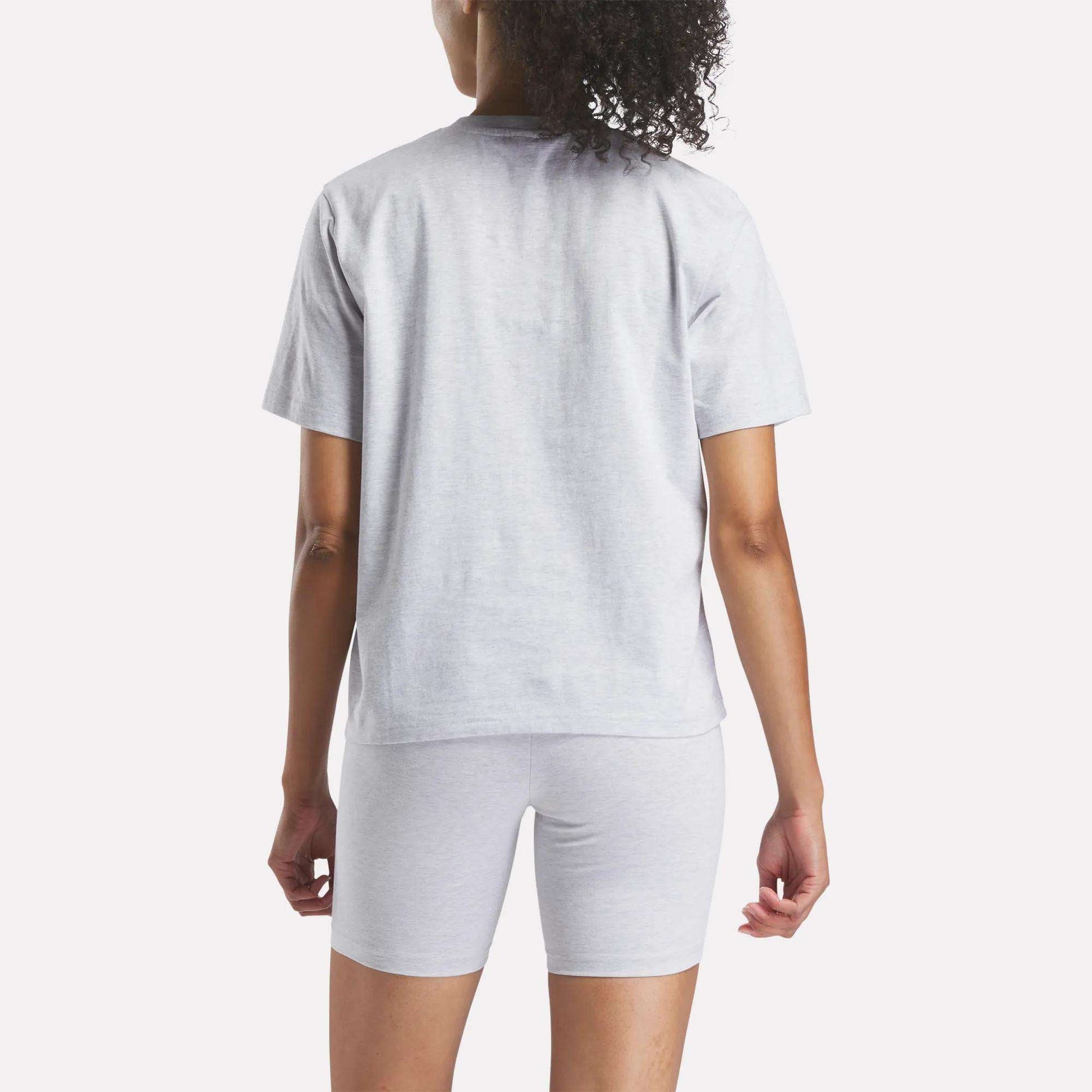 A person with curly hair is seen from behind wearing a light gray Reebok Women's Big Logo Oversized Crew Short Sleeve Tee against a plain white background.