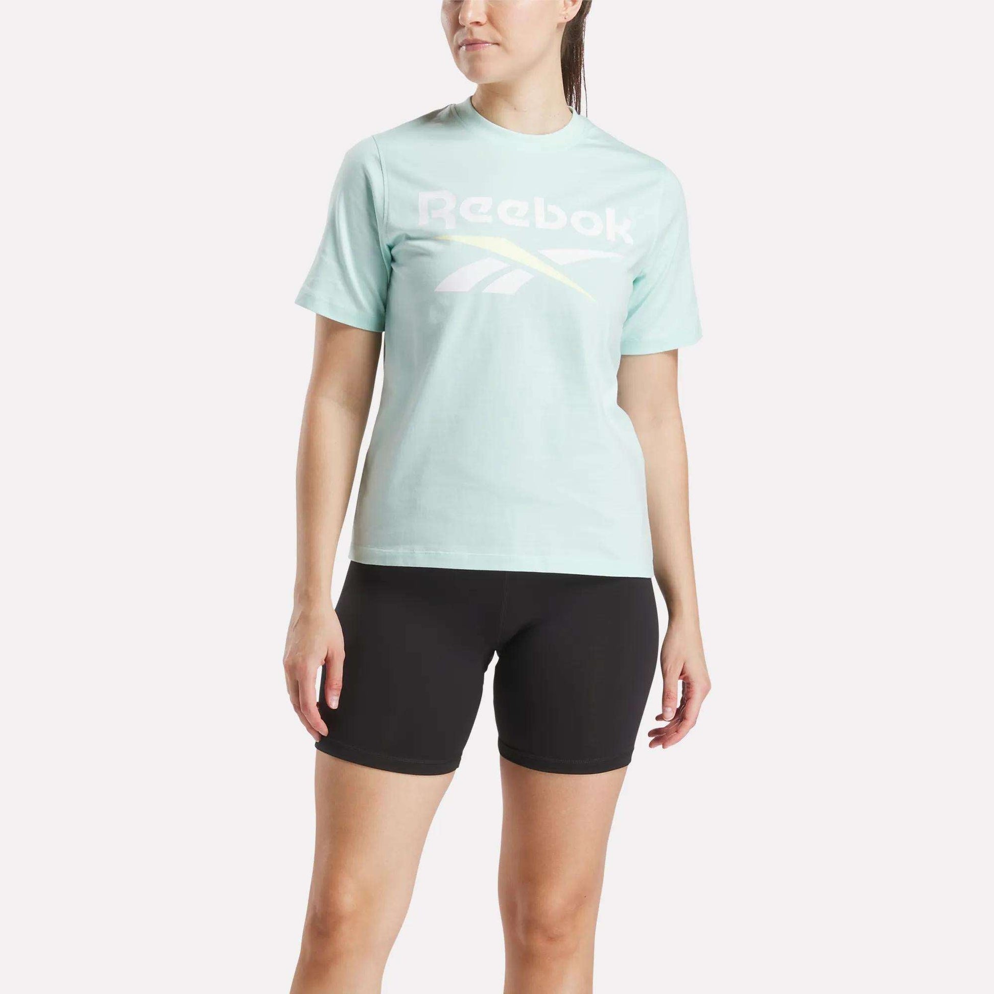 A woman wearing the Reebok Women's Two-Color Logo Crew Short Sleeve Tee in green.