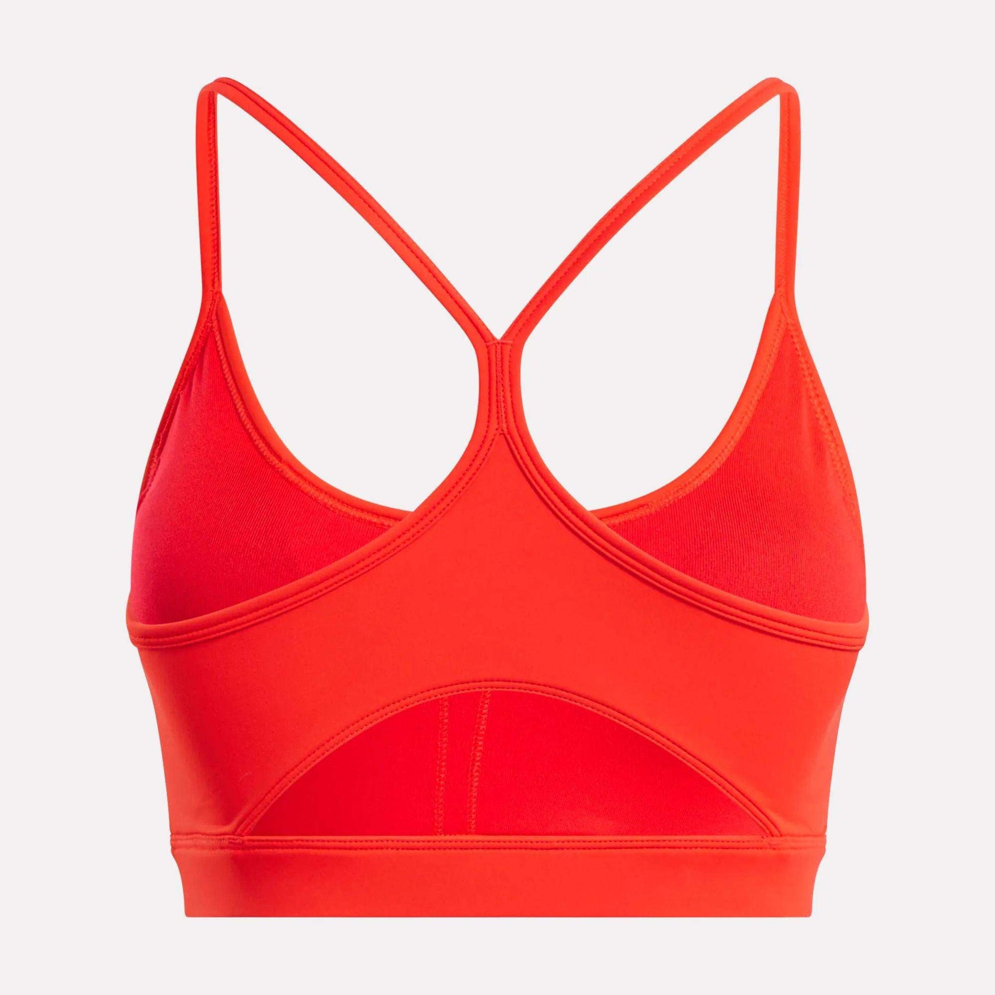The Reebok Women's Core Strappy Bra - Medium Support in bright red features thin crisscross racerback straps, dries quickly, and is ideal for medium-impact workouts. Shown from the back on a plain white background.