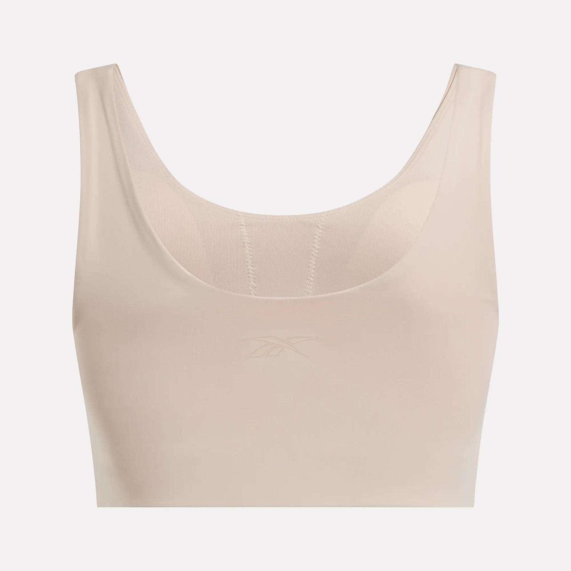 The Reebok Women's Yoga V-Neck Bra in beige features a sleeveless, seamless design with medium-impact support, a scoop neckline, and a subtle front logo. Ideal for studio workouts. Set against a plain white background.