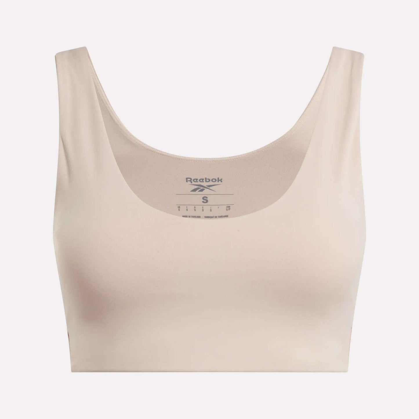 The Reebok Women's Yoga V-Neck Bra in beige features a scoop neckline and wide straps, offering medium-impact support for studio workouts. The Reebok logo and sizing appear inside the neckline on a plain light background.