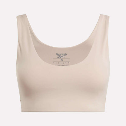 The Reebok Women's Yoga V-Neck Bra in beige features a scoop neckline and wide straps, offering medium-impact support for studio workouts. The Reebok logo and sizing appear inside the neckline on a plain light background.