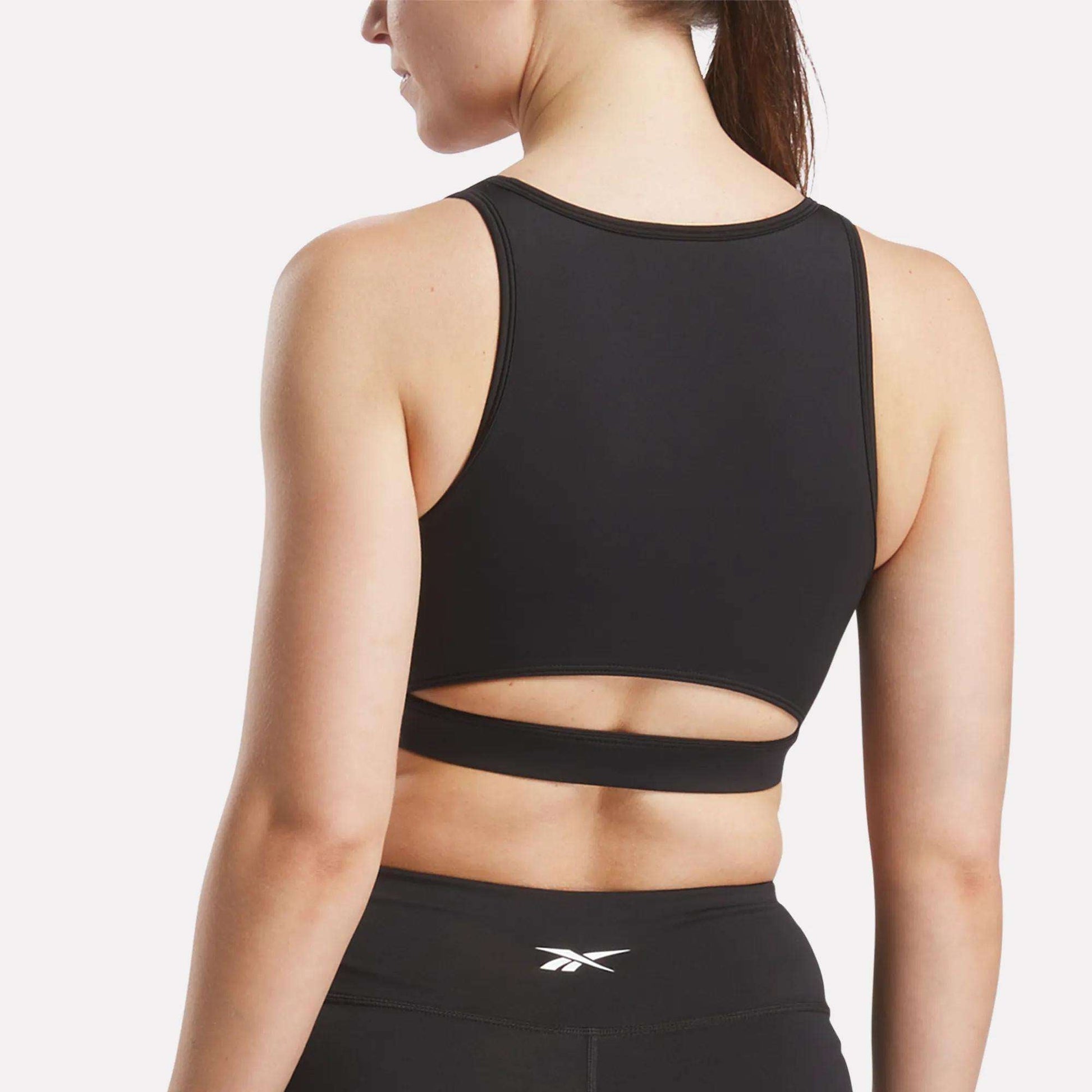 A woman wears the Reebok Women's Core High-Impact Bra with a cutout back and matching sweat-wicking leggings, shown from behind against a plain white background.
