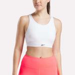 A woman wears the Reebok Women's Core High-Impact Bra and high-waisted neon pink workout leggings, standing against a plain light background with her face partially out of frame.