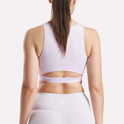 A woman is shown from the back wearing Reebok's Women's Core High-Impact Bra in light pink, featuring sweat-wicking fabric and a stylish cut-out above the waistband. Perfect for high-impact training, it pairs with matching leggings.