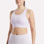 A woman models the Reebok Women's Core High-Impact Bra in lavender, paired with matching high-waisted leggings. She stands against a plain white background, shown from shoulders to hips with her head slightly turned.