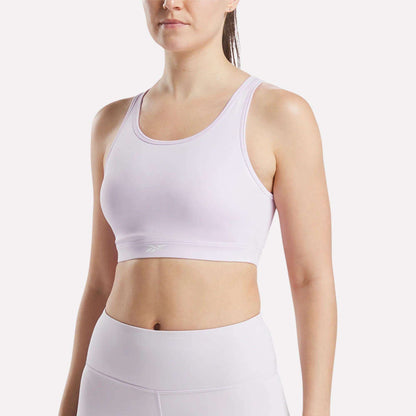 A woman models the Reebok Women's Core High-Impact Bra in lavender, paired with matching high-waisted leggings. She stands against a plain white background, shown from shoulders to hips with her head slightly turned.