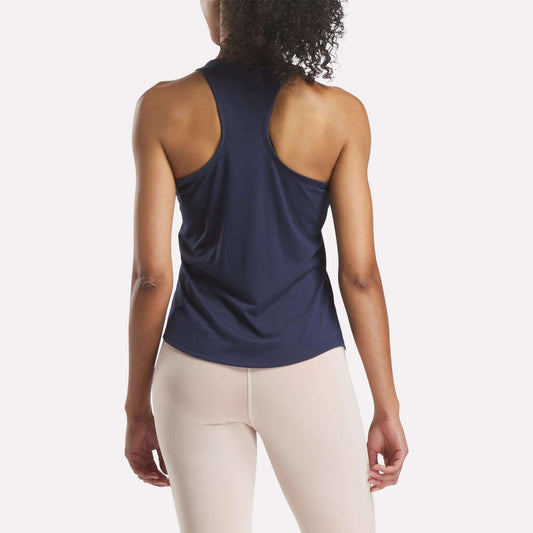 A woman, facing away from the camera, wears a Reebok Women's Core Tank Top (slim fit) in navy blue with light beige leggings, set against a plain white background.