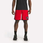 A person wearing a black shirt, Reebok Men's Basketball Mesh Shorts in red with RBK-DRY tech and a patch on the left leg, black socks, and black sneakers stands against a plain white background.