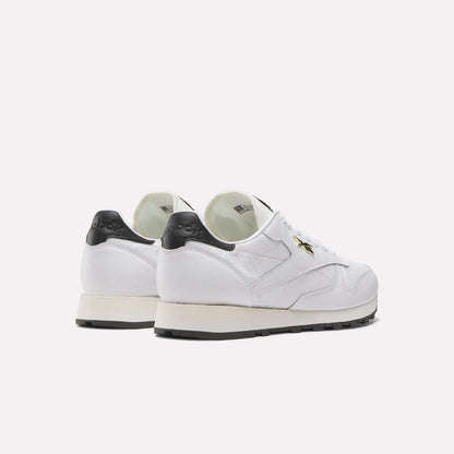 The Reebok Classic Leather Shoes feature a white leather upper, black heel accents and soles, plus a gold star detail on the side, reflecting retro running style. Displayed on a plain white background.