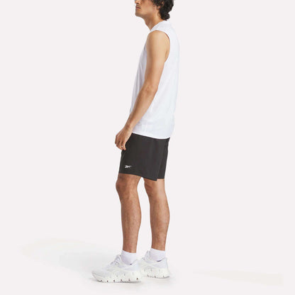 A man stands sideways against a plain white background, wearing a Men's Sleeveless Tech Training T-Shirt by Reebok, black shorts, and white athletic shoes.