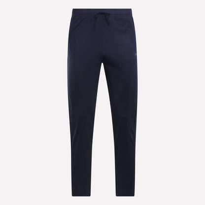 Reebok Men's Train Knit Pants in navy blue, featuring a slim fit jogger style with an elastic waistband and drawstring. Displayed against a plain light background, these gym pants have no visible logos or patterns.