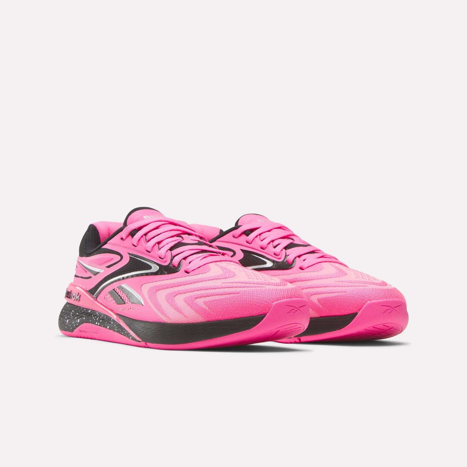 The Women's Nano X5 Edge Training Shoes by Reebok feature a bright pink design with black and silver accents, a textured sole, and modern style—ideal for HIIT—shown on a plain white background.
