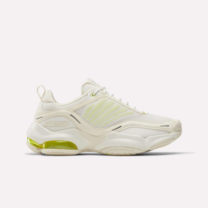 The Reebok Women's DMX Series 3000 Training Shoes are white athletic sneakers with light yellow accents, mesh panels, and a chunky sole featuring a visible green heel air cushion and DMX 3 Technology for advanced comfort.