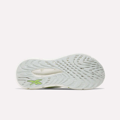 The image shows the bottom of a white Women's FloatZig Double Running Shoe by Reebok, featuring a wavy tread pattern and a small green logo near the heel, designed for maximum cushioning on long runs.