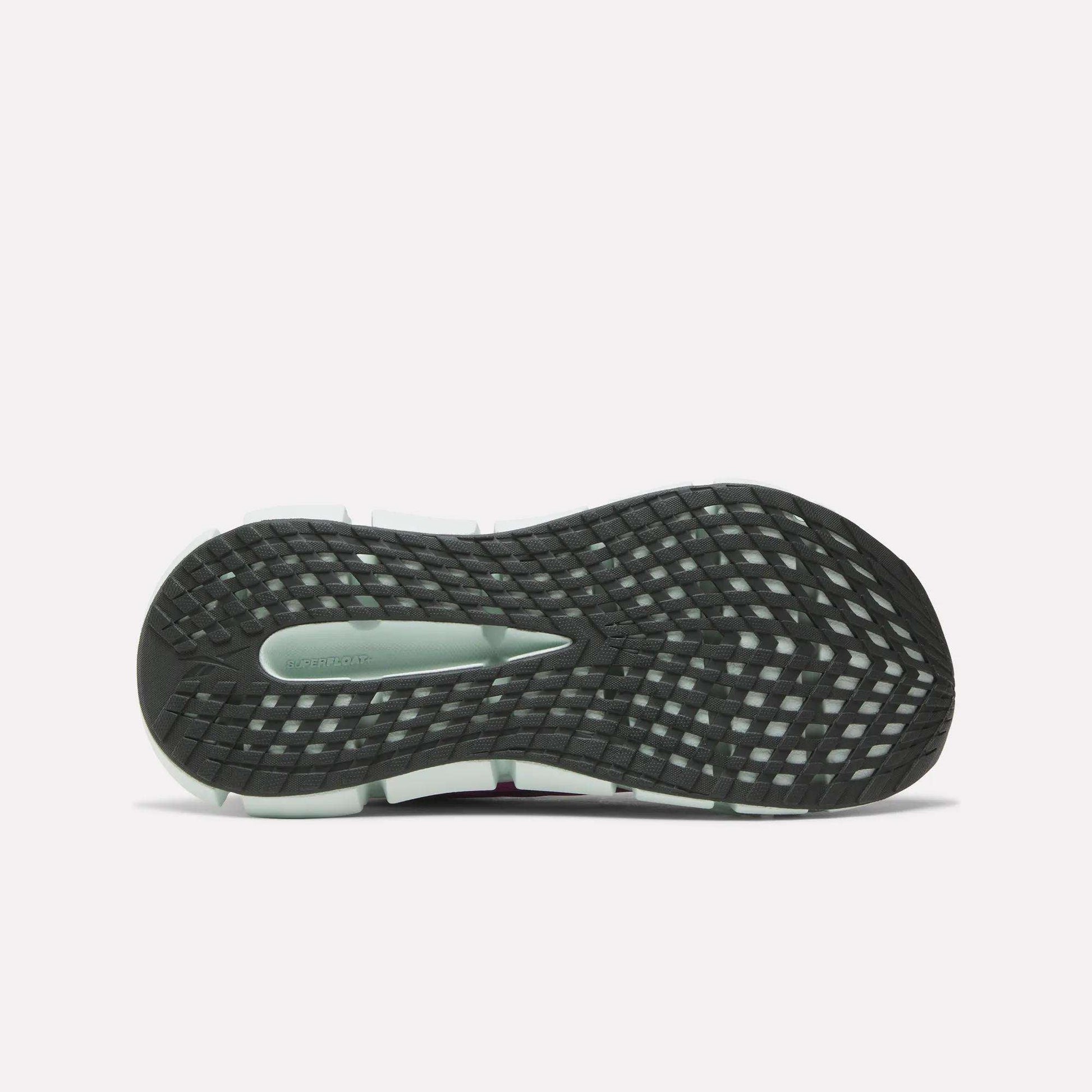 The image displays the bottom of the Reebok Women's FloatZig 2 Running Shoe, featuring a black sole with a grid-like traction pattern, energy-returning cushioning, and a gray section near the heel.