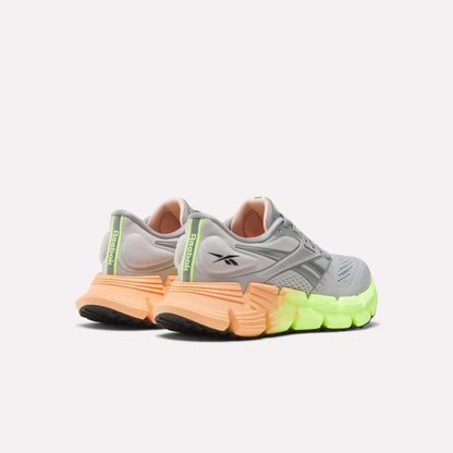The Reebok Women's FloatZig 2 Running Shoes in gray feature black logos, Superfloat+ cushioning, and thick gradient soles from orange at the heel to neon yellow at the front, shown from the back and side on a white background.