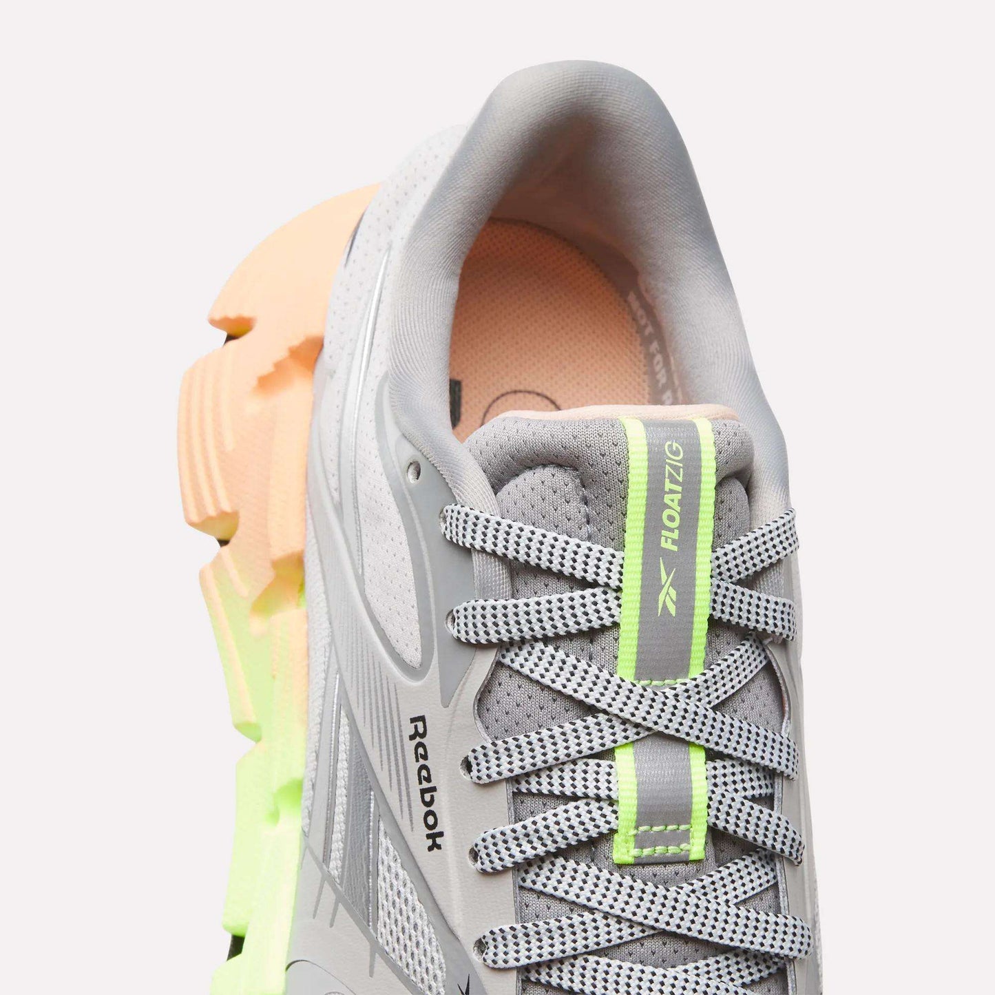 Close-up of Reebok Women's FloatZig 2 Running Shoes in gray with light green and gray laces, neon green accents, and an orange and green chunky sole. Features FLOATZIG branding and Superfloat+ cushioning for enhanced comfort.