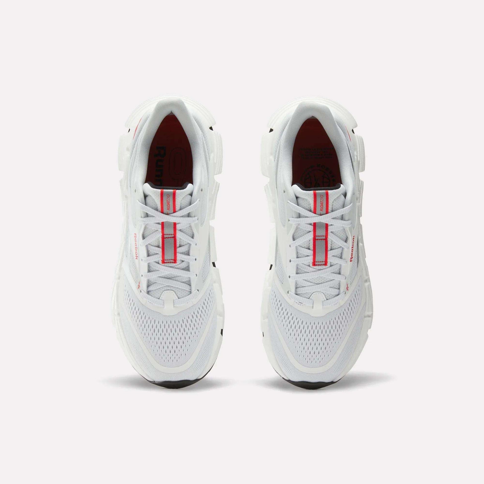 A pair of Reebok Men's FloatZig 2 Running Shoes in white, shown from above with red accents on the tongue and mesh details on the toe, placed side by side on a plain light background.