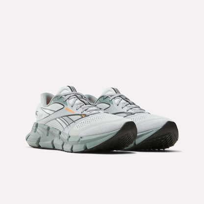 The Reebok Men's FloatZig 2 Running Shoes in white and light gray feature supportive uppers, black soles, orange accents, green detailing, and Superfloat+ cushioning, shown on a plain white background.