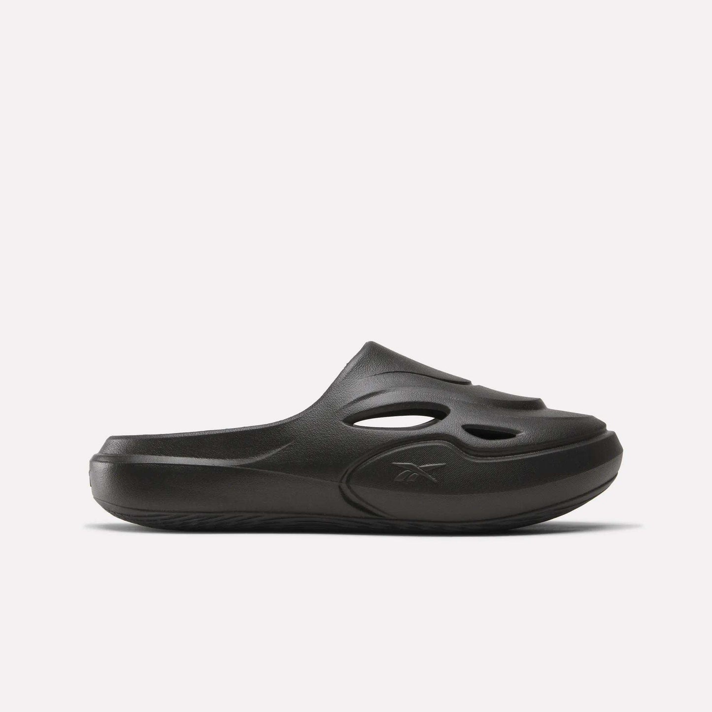 The Reebok DMX Recovery Mules are black slip-on shoes made from molded EVA, with cutout vents on the upper, a closed toe, and a chunky sole. Shown in side profile against a plain white background.