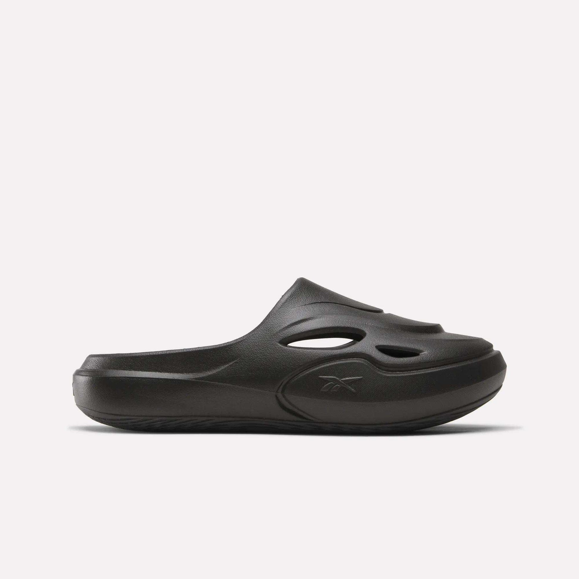 The Reebok DMX Recovery Mules are black slip-on shoes made from molded EVA, with cutout vents on the upper, a closed toe, and a chunky sole. Shown in side profile against a plain white background.