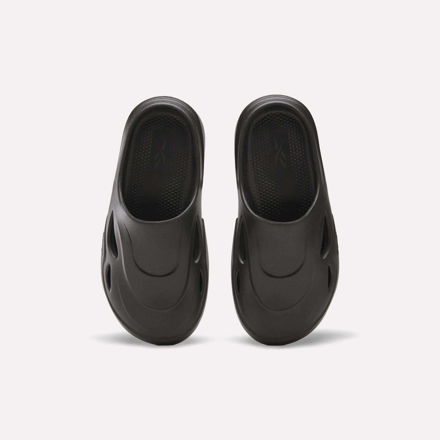 The Reebok DMX Recovery Mules are black, molded EVA slip-ons with DMX Moving Air tech, a textured footbed, and oval side vents, displayed from above on a white background.