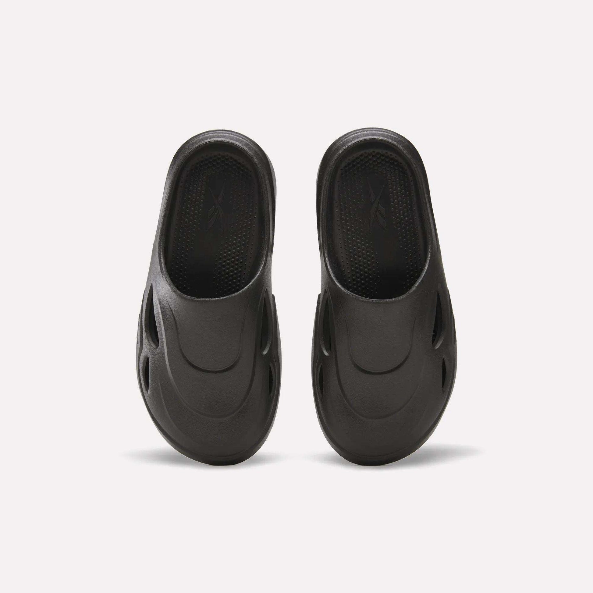 The Reebok DMX Recovery Mules are black, molded EVA slip-ons with DMX Moving Air tech, a textured footbed, and oval side vents, displayed from above on a white background.