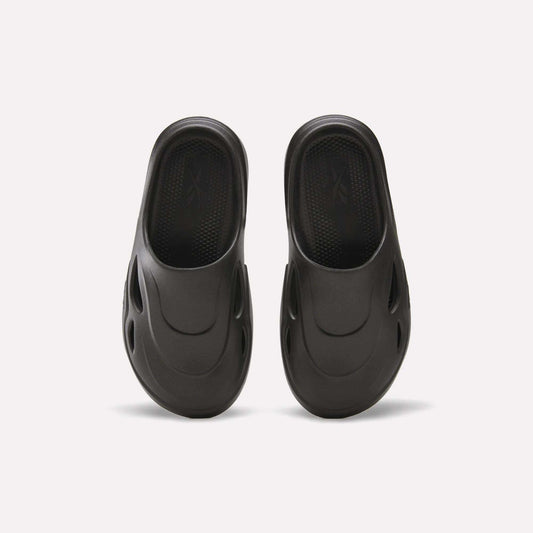 The Reebok DMX Recovery Mules are black, molded EVA slip-ons with DMX Moving Air tech, a textured footbed, and oval side vents, displayed from above on a white background.