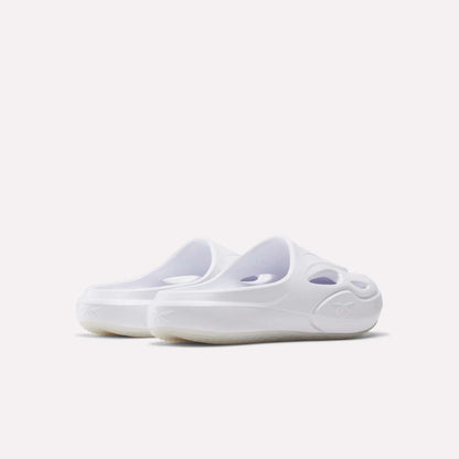A pair of Reebok DMX Recovery Mules in white, featuring a slip-on design, molded EVA construction, cut-out details, and rounded toes is shown from an angled rear view on a plain white background.