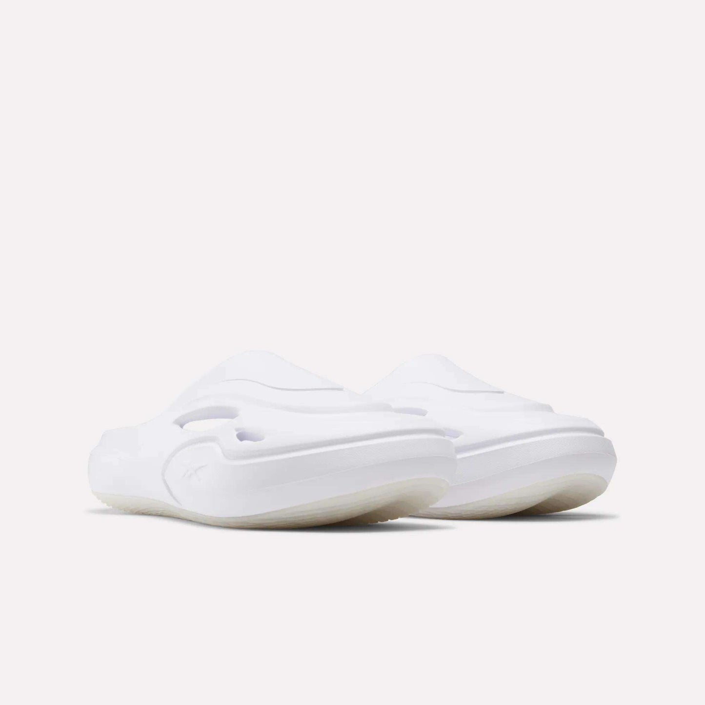 A pair of Reebok DMX Recovery Mules in white with a minimalist, slip-on design and thick molded EVA soles, displayed on a plain light background.