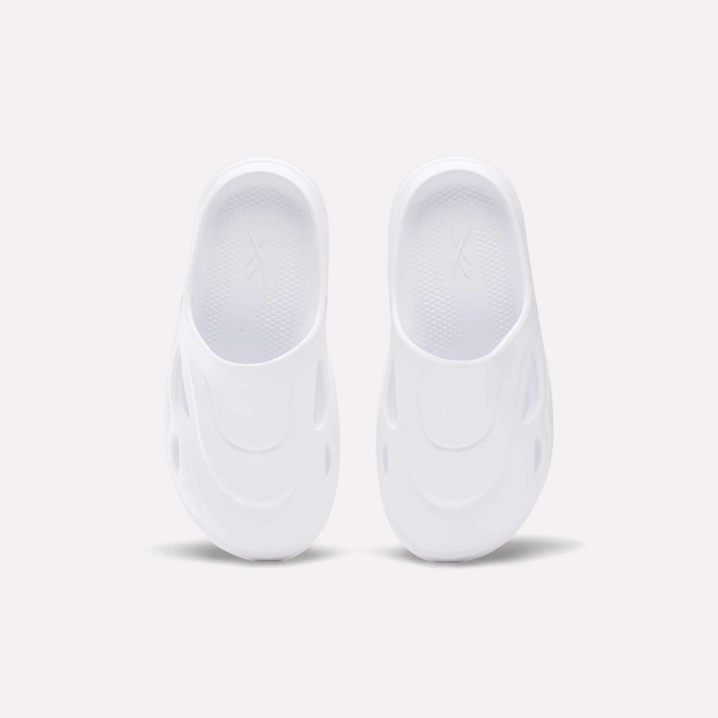 The Reebok DMX Recovery Mules are white slip-on shoes featuring a futuristic design with oval side cutouts, crafted from molded EVA, shown from above on a plain light background.