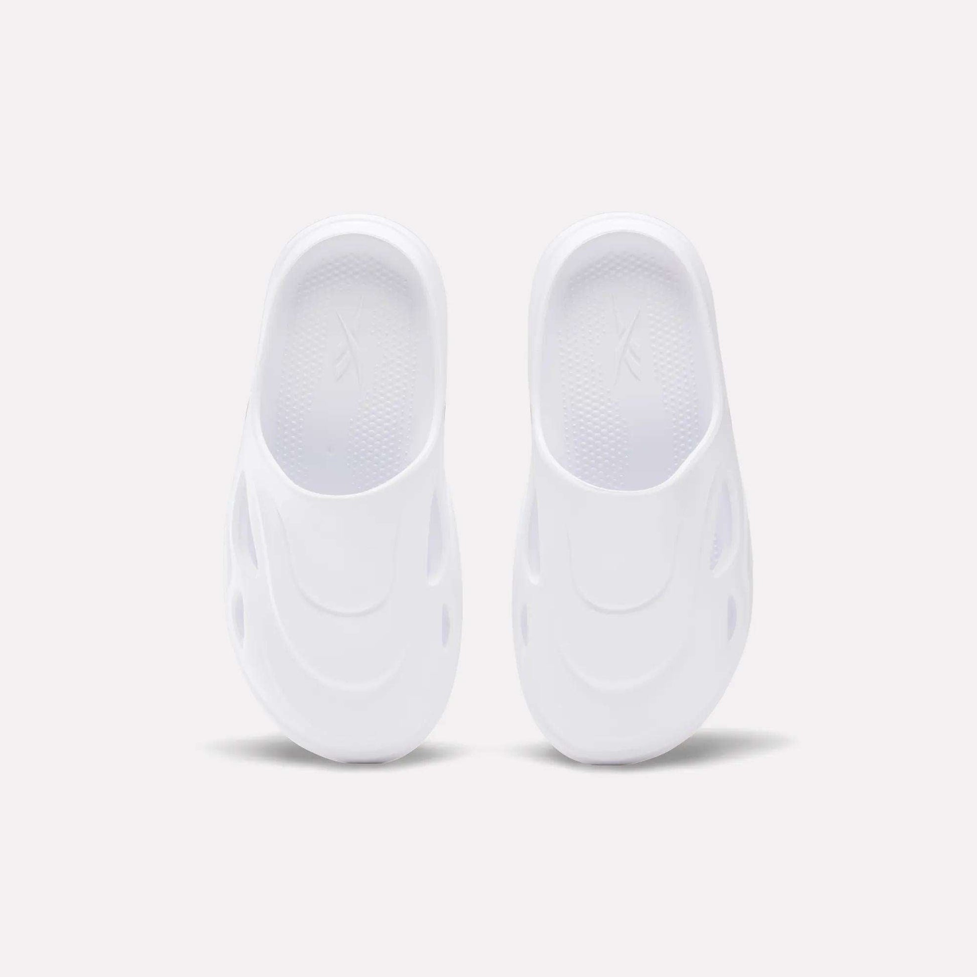 The Reebok DMX Recovery Mules are white slip-on shoes featuring a futuristic design with oval side cutouts, crafted from molded EVA, shown from above on a plain light background.