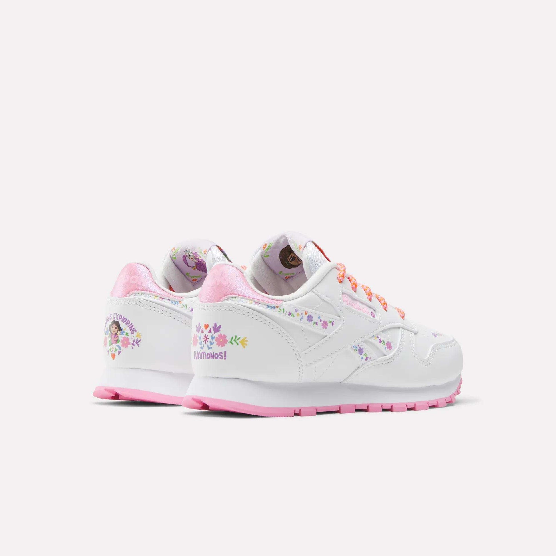 The Reebok x DORA Classic Leather Shoes for little kids feature a white design with pink soles and laces, floral graphics, and Dora the Explorer character details. These comfy Reebok shoes have a soft pink interior lining, perfect for young fans.
