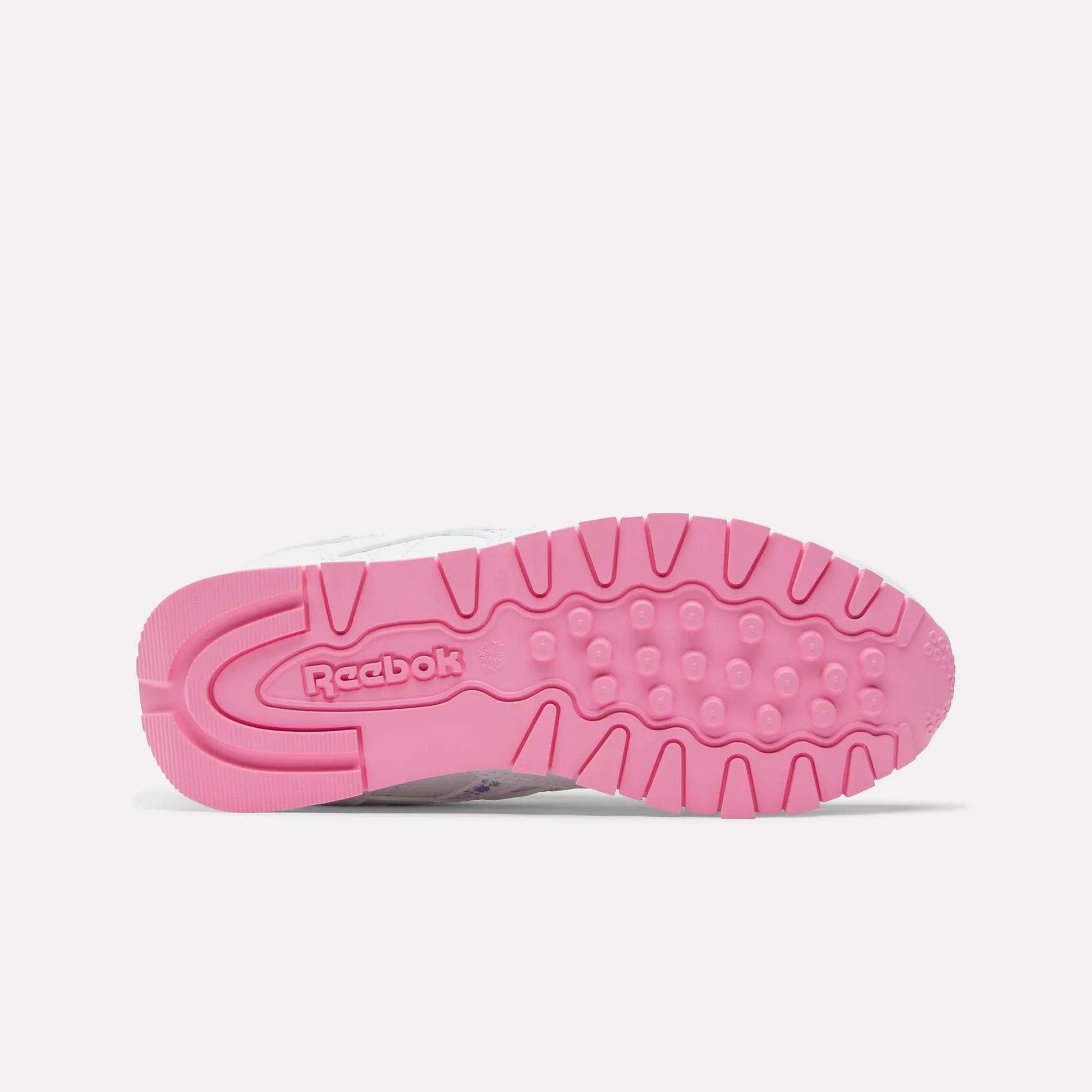 Bottom view of Reebok x DORA Classic Leather Shoes for little kids, showcasing a bright pink textured outsole with the Reebok logo near the heel. This vibrant style stands out against a plain white background—ideal for young sneaker fans.