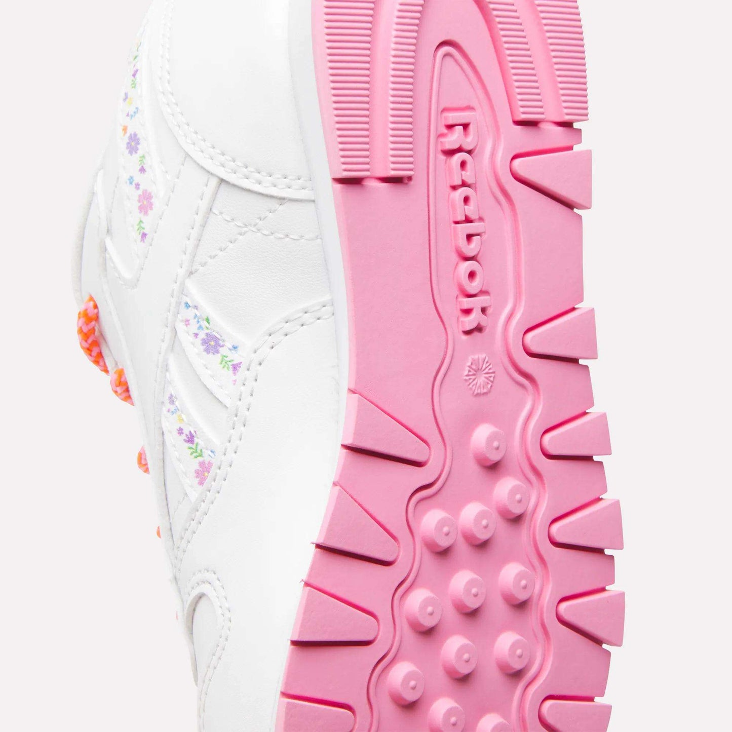 Close-up of the sole of white Reebok x DORA Classic Leather Shoes for little kids with pink tread and pastel floral details—perfect comfy sneakers for stylish young explorers. The Reebok logo is visible on the side.