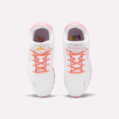 The Reebok x DORA Classic Leather Shoes for little kids feature pink accents, orange patterned laces, and colorful floral designs on the toe and tongue, shown from above on a plain light background.