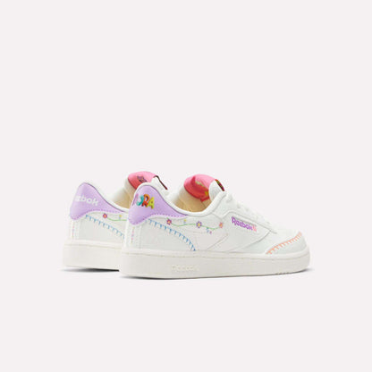 The Reebok x DORA Club C Shoes for little kids feature a white base with pastel rainbow details, embroidered accents, colorful heel designs, multicolored stitching, and bold Reebok branding for a playful standout look.