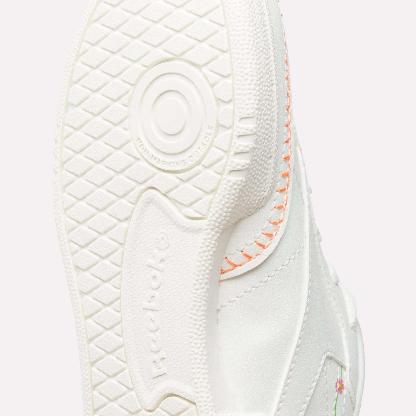 Close-up of the sole on Reebok x DORA Club C Shoes for little kids, showing textured grip, circular pattern, orange stitching, and a hint of a floral design on the upper.